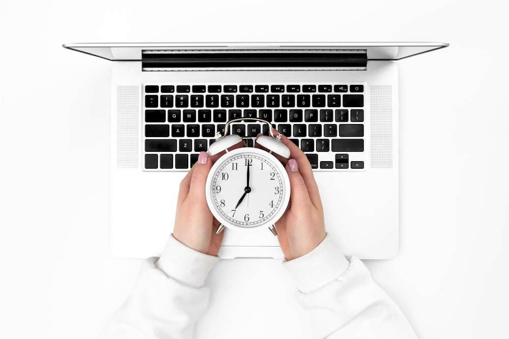 Manos sosteniendo un reloj despertador blanco sobre el teclado de una laptop